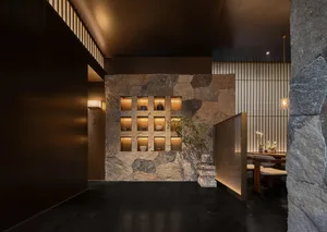 Dining room with a stone wall and floor, a modern dining table and chairs, vases, and dim lighting creating a cozy atmosphere