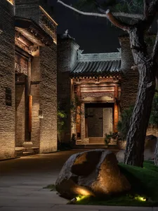 一座傳統中國建築的石材外牆，擁有大型拱門和石板路，低調的光源下