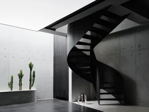A dimly lit room with a modern metal staircase in a spiral design, set against a concrete floor