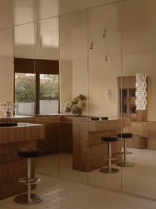 Modern kitchen and dining space with a large island, wooden furniture, and glass accents, decorated with a potted plant and vases, lit by natural sunlight