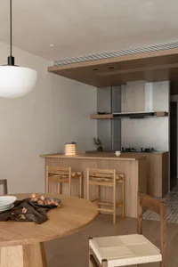 Modern kitchen with wooden cabinets and dining table, featuring a stove top oven and sink, with soft warm lighting creating a cozy atmosphere