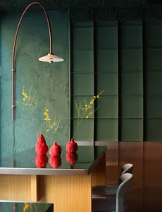 A modern living room with a green accent wall, a dining table, and comfortable seating, decorated with flowers and a potted plant
