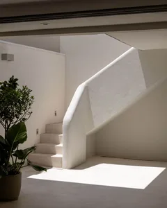 A white staircase in a sunlit area with a concrete staircase and white railing
