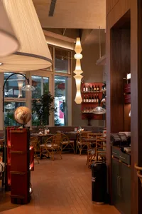 Cozy restaurant dining area with multiple tables, chairs, potted plants, and dim lighting, featuring a combination of wood and metal elements