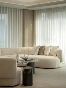A well-lit living room with a white couch, a glass table, and two vases, surrounded by white walls and natural light