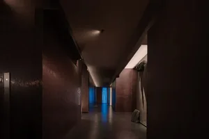 A dimly lit stone hallway with a narrow corridor, a doorway, and a suitcase on the floor