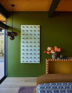 Cozy living room with green walls, a wooden counter, and a white wall hanging with a row of circles, featuring a vase with flowers