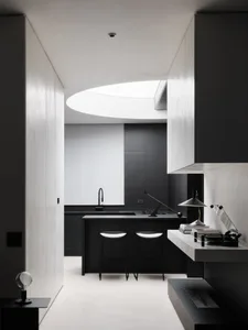 A dimly lit modern kitchen with a black counter and sink under a window, surrounded by three black and white chairs