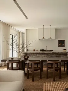 Modern kitchen with a marble countertop, wooden floor, and natural light from windows, featuring a center island and dining area