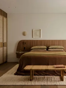 Cozy bedroom with a brown bed, table, and chair, surrounded by warm wood tones and natural light