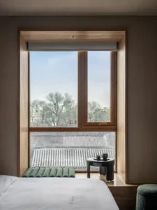 Cozy modern bedroom with a large window, a bed, and natural light, decorated with a vase and a bowl, and a chair and dining table