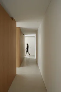 A woman walks down a dimly lit hallway with a wood finish and grey tile floor, creating a calm atmosphere