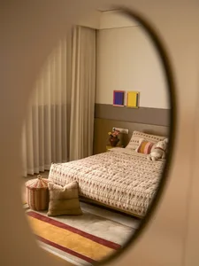 Cozy bedroom with a white comforter and brown blanket, a mirror above the bed, and a rug on the floor