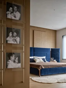 A modern bedroom with a blue bed, wooden headboard, and wooden floor, lit by natural light