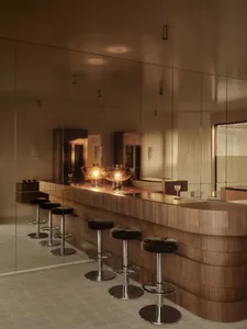Modern bar area with a wooden counter, large mirror, and glass wall, dimly lit for a cozy atmosphere