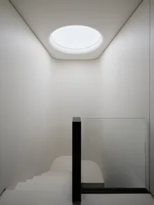 A dimly lit room with a central staircase made of concrete and a black railing, surrounded by empty space