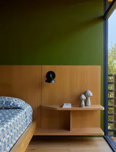 A modern bedroom with a bed, nightstand, and a green accent wall, lit by natural sunlight through a window, creating a calm and inviting atmosphere