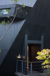 一張黑白照片，拍攝了一個獨特形狀的現代房屋，屋頂斜坡，屋內有大型窗戶，整體由木材所製成
