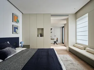 A modern bedroom with a gray color scheme, a blue blanket, and natural light from a window, featuring a bed and a bench in a well-organized and comfortable space