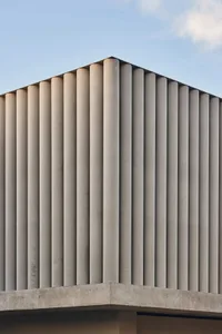 Photograph of a modern building with a white concrete facade, featuring a row of vertical windows and natural light from above