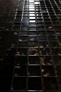 A dimly lit black and white photograph of a tile floor, possibly in a bathroom, with a minimalist and functional style