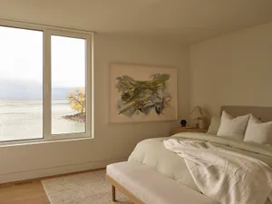 A well-lit bedroom with a bed, window, and abstract painting, featuring wood and white walls