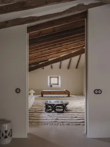 Cozy living room with a wooden floor, a white wall, a couch, a chair, and a dining table, with natural lighting and wooden elements creating a warm and comfortable space
