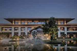 A serene modern building with a glass facade and a pond surrounded by trees, set against a soft and diffused light background
