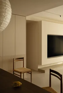 一間充滿光線的現代客廳，設有平面電視、餐桌和木製家具，背景為白牆