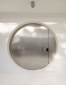 A modern doorway with a circular metal door in a white hallway, lit by natural daylight