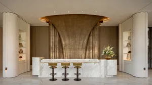 Modern hotel lobby with a marble countertop, curved wall, and soft lighting, featuring a row of stools and a vase with flowers