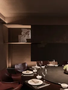 A dimly lit dining room with a large wooden dining table set for a meal, surrounded by chairs and a vase, creating a cozy atmosphere