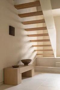 A modern staircase with a wooden railing and table, set against a white background, with a bowl on the table