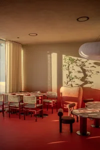 Cozy modern dining and living space with wood tables and chairs, metal couch and chair frames, and a potted plant, lit by soft warm lighting