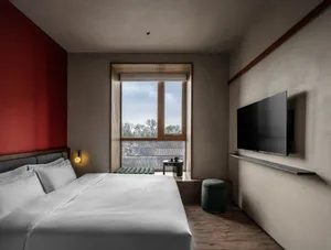 Cozy bedroom with a red accent wall, a white bedspread, and a TV on a side table near a window