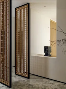 A well-lit living room with a white wall, a wooden door with decorative design, and a large window