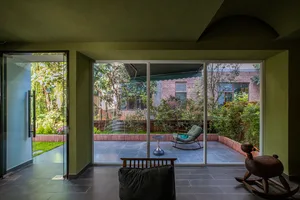Comfortable living space with a couch, chair, and dining table, surrounded by natural light and greenery, with wood and glass materials