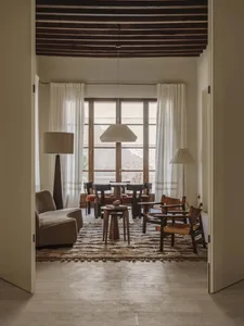 A well-lit living room with a couch, chair, dining table, and multiple chairs, decorated with a rug and lamp, creating a warm and inviting atmosphere