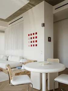A well-lit living room with a white couch, a dining table, and a chair, featuring wood and white furniture in a clean and modern aesthetic