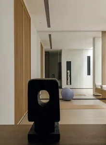 A modern art gallery with a wooden floor, featuring a black sculpture, a purple ball, and a bench in a black and white space with a timeless and elegant atmosphere