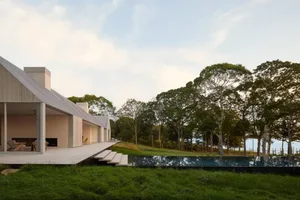 A modern house with a large pool surrounded by trees in a grassy area