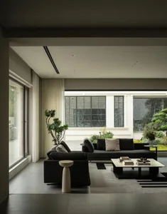 A modern living room with a black leather couch, chair, and glass coffee table, surrounded by clean lines and minimal decor, with natural light pouring in through a large window
