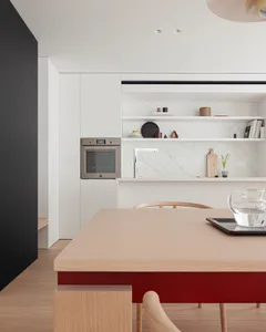Modern kitchen with a wooden table and chairs, featuring a stove, oven, sink, and refrigerator, with natural light and a vase on the table