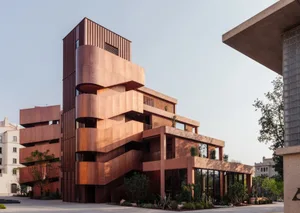 Modern building with a curved design, featuring a mix of red and brown tones, concrete, and glass, set in a city environment with natural light and urban surroundings