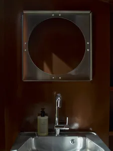Small private bathroom with a metal sink and circular mirror, brown color scheme, and natural lighting