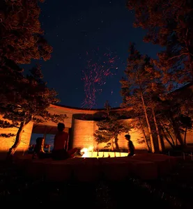 A group of people sitting around a stone fire pit in a forest, surrounded by natural scenery and enjoying each other's company