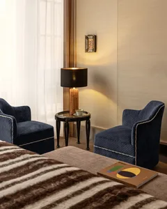 A well-lit living room with two blue chairs on a rug in front of a table with a lamp, creating a cozy and inviting atmosphere