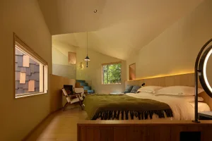 A well-lit bedroom with a wooden floor, a bed, a chair, and a window, creating a comfortable atmosphere