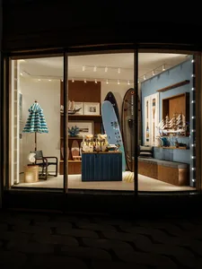 A surfboard and sailboat are displayed in a store with a blue and white color scheme, creating a nautical theme, under dim lighting