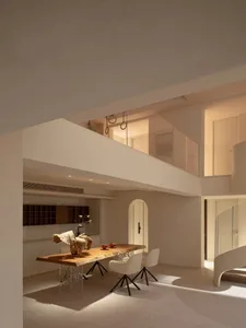 Modern kitchen with a wooden dining table, chairs, vases, and a clean minimalist design, featuring a sink and oven, with soft and diffused lighting